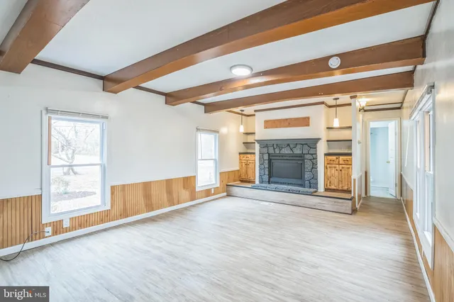 a view of an empty room with wooden floor fireplace and a window