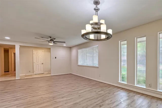 an empty room with wooden floor chandelier and windows