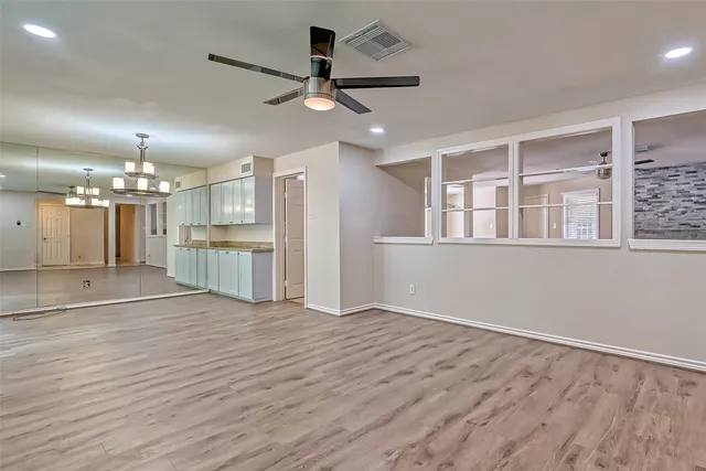 a view of an empty room with wooden floor and a kitchen
