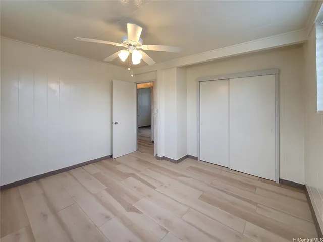 a view of an empty room with wooden floor and a ceiling fan