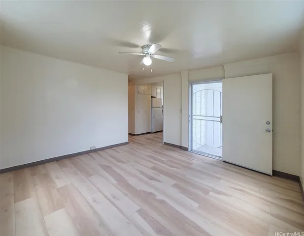 a view of an empty room with wooden floor and a ceiling fan