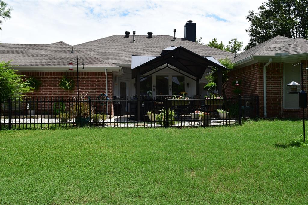 4201 Glistening Spring Rowlett, TX 75088 - Photo 30 of 33 Rear exterior featuring a brick facade, shingle roof, and a covered patio area with a black metal fence