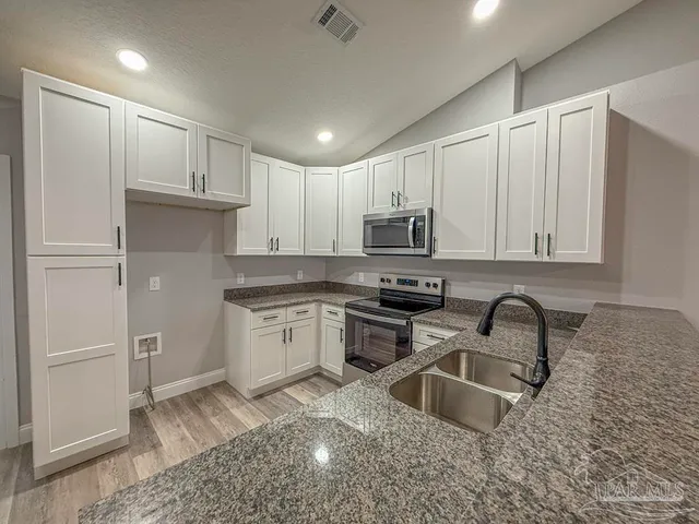 a kitchen with granite countertop a sink a stove a refrigerator and cabinets
