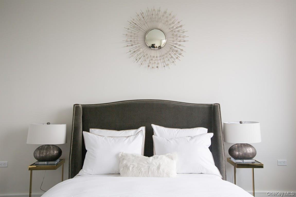 1 3rd, Unit 825 Mineola, NY 11501 - Photo 11 of 25 a bed in a room with a lamp and a large mirror