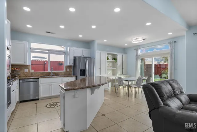 a large kitchen with granite countertop lots of white cabinets a sink a stove a dining table and chairs