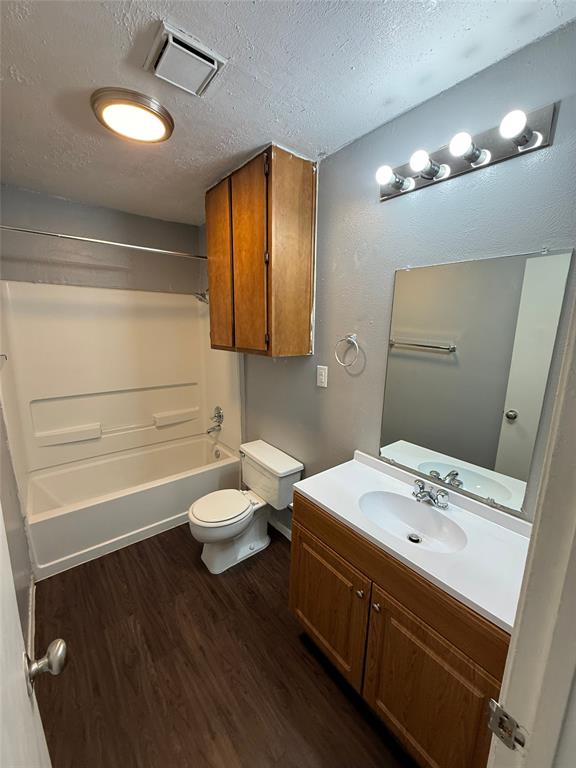 1714 Short Street, Unit D Cleburne, TX 76033 - Photo 6 of 9 Full bathroom featuring wood-finish flooring, a white tub and shower combination, a single vanity with a white countertop and integrated sink, and a mirrored wall