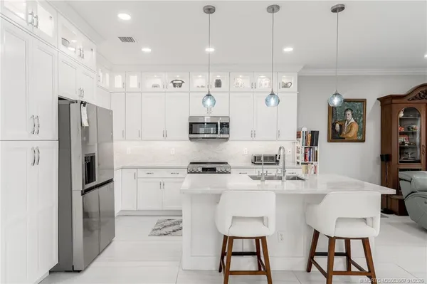 a kitchen with stainless steel appliances kitchen island granite countertop a dining table chairs refrigerator and sink