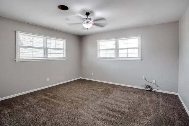 an empty room with chandelier fan and windows