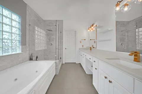 a spacious bathroom with a granite countertop double vanity sink a mirror a bathtub and next to a window