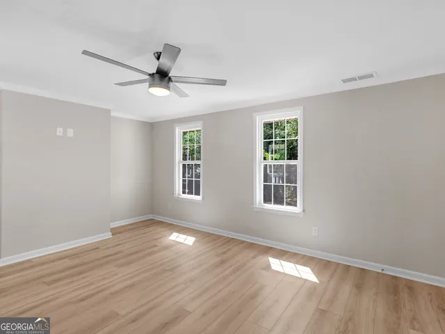 a view of empty room with wooden floor and fan