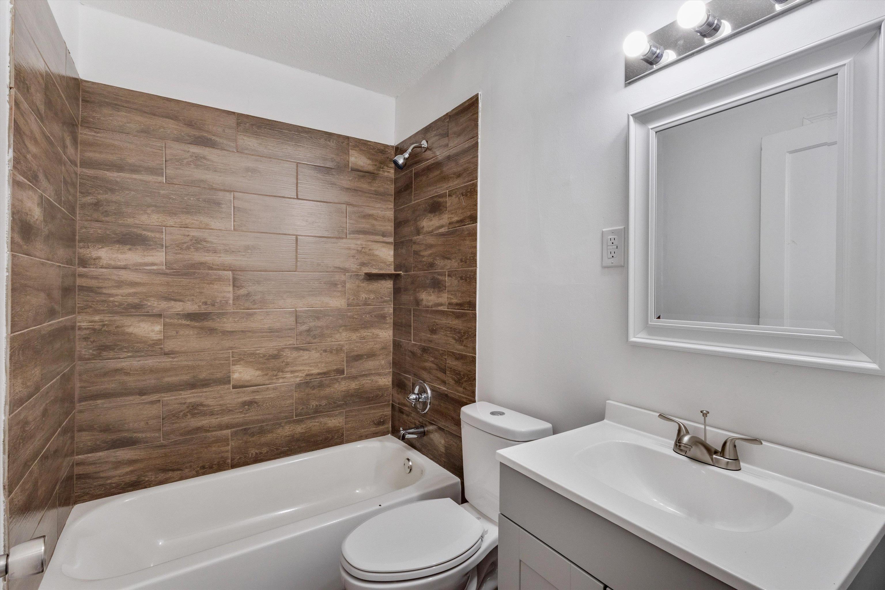 4565 Verne Road Memphis, TN 38117 - Photo 15 of 18 Bathroom featuring a white bathtub, wood-finish tile shower surround with integrated shelf, white toilet, and a vanity with a white countertop, undermount sink, and brushed nickel faucet
