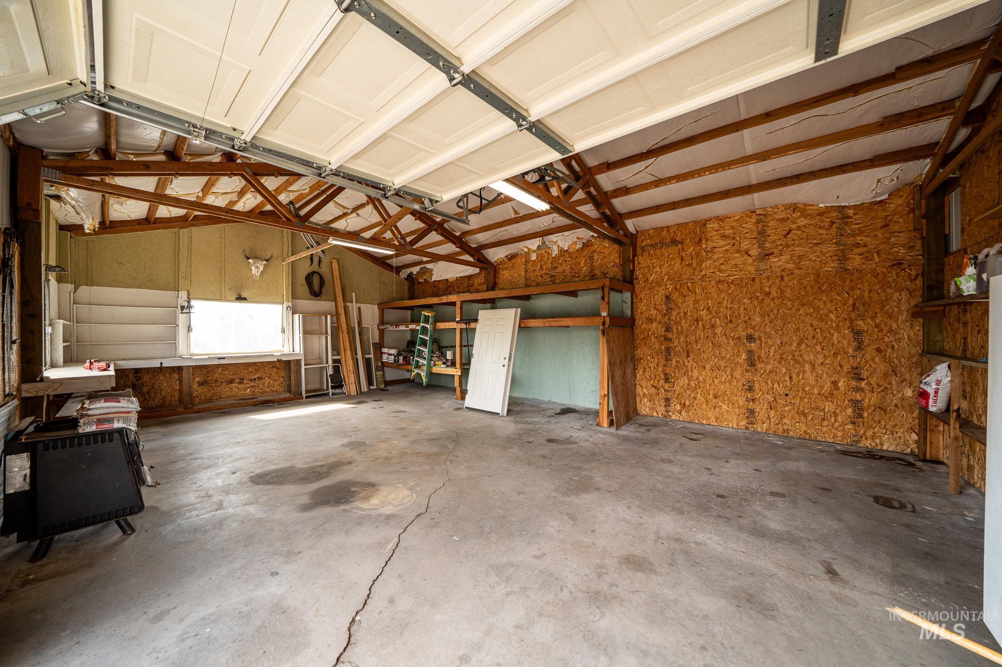161 Saddle Ridge Road White Bird, ID 83554 - Photo 8 of 49 Spacious garage with exposed wood rafters, concrete flooring, built-in shelving, a large window, and double garage doors