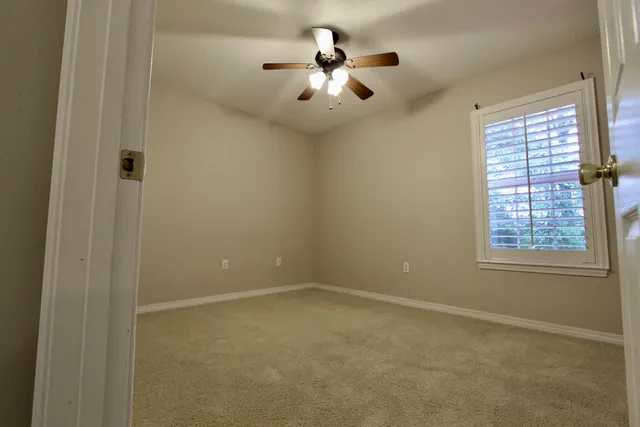 an empty room with chandelier fan and windows