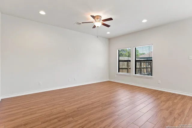 a view of an empty room with wooden floor and a ceiling fan