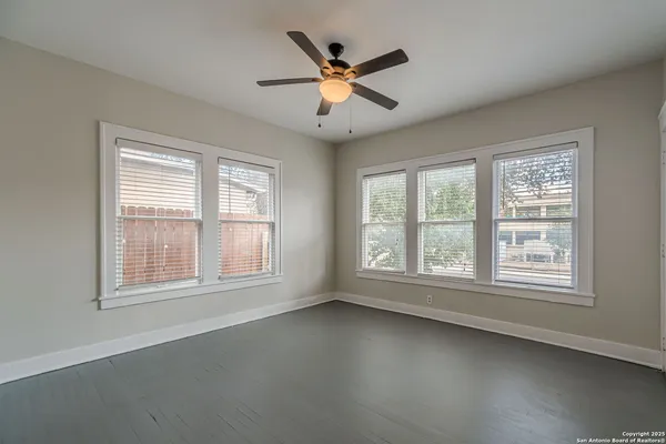 an empty room with chandelier fan and windows