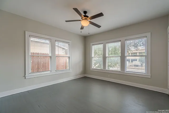an empty room with chandelier fan and windows