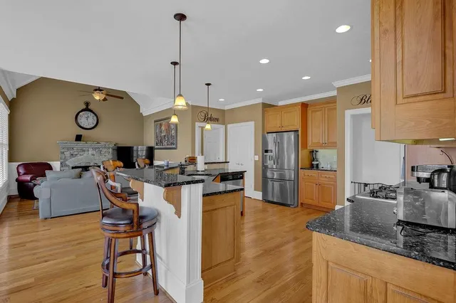 a kitchen with stainless steel appliances granite countertop a refrigerator a sink dishwasher a stove and a dining table with wooden floor