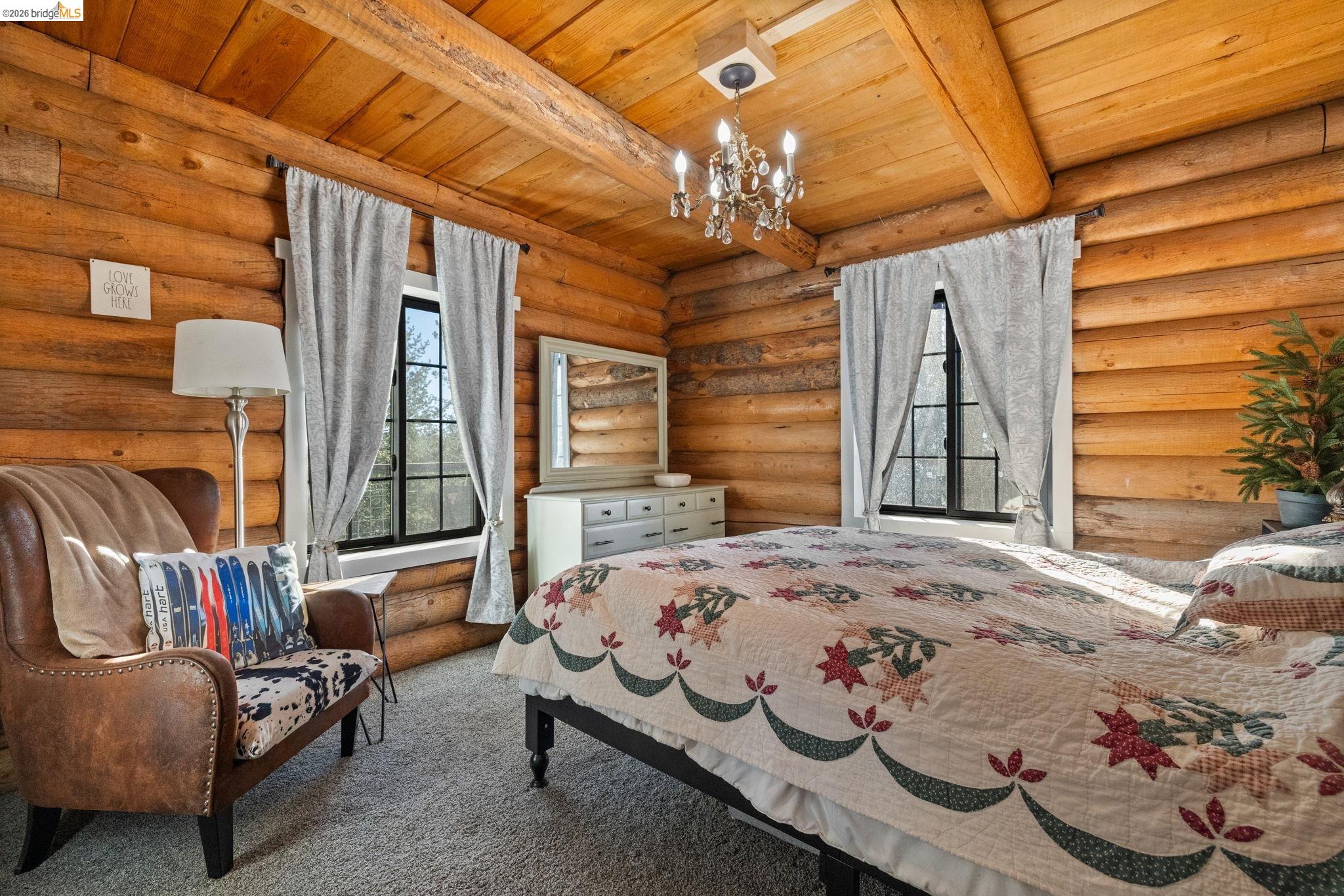 16144 Big Hill Road Sonora, CA 95370 - Photo 22 of 51 Log cabin interior featuring exposed log walls, a vaulted wood plank ceiling with exposed log beams, and a chandelier light fixture