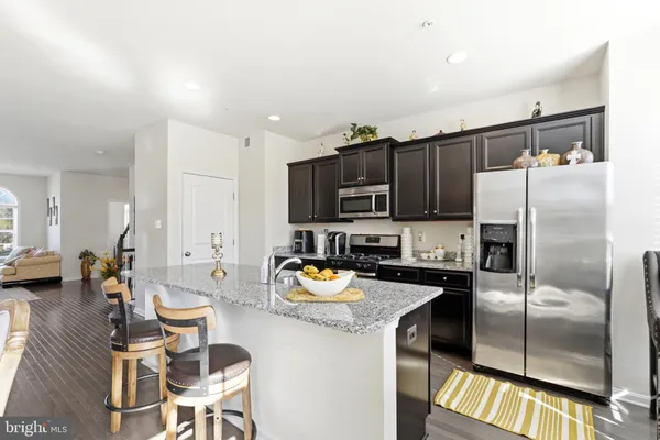 a kitchen with stainless steel appliances granite countertop a refrigerator a stove a sink a dining table and chairs with wooden floor
