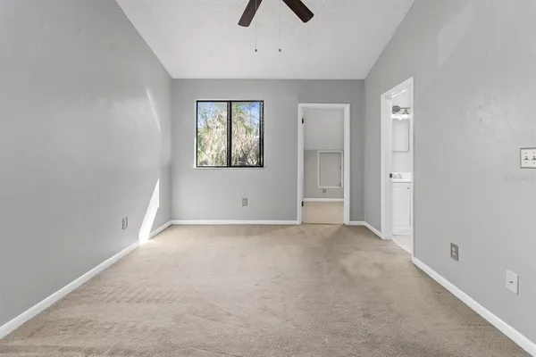 an empty room with chandelier fan and windows