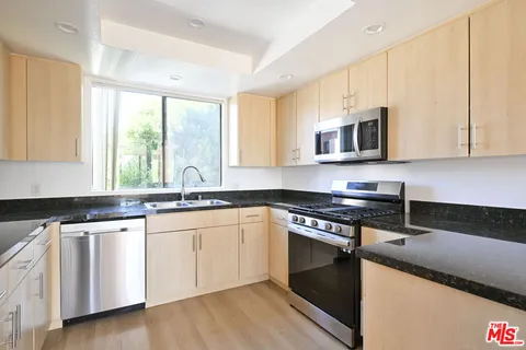 a kitchen with granite countertop a sink cabinets stainless steel appliances and a window