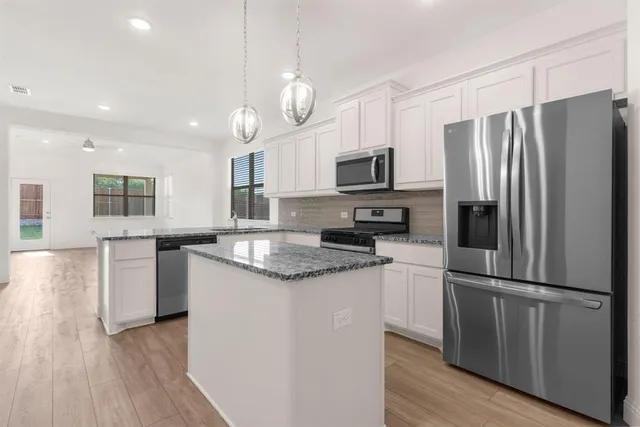 a kitchen with kitchen island granite countertop stainless steel appliances a refrigerator a stove top oven and a center island with wooden floor