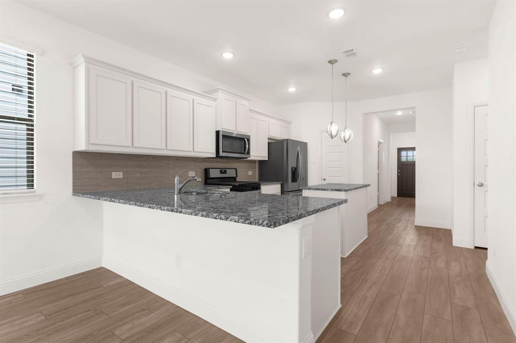216 Town Pk Avenue Princeton, TX 75407 - Photo 7 of 19 a kitchen with kitchen island granite countertop a sink a stove a microwave a refrigerator and white cabinets with wooden floor