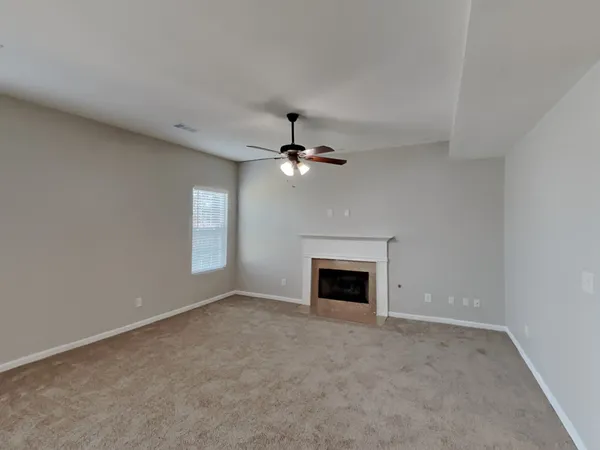 an empty room with chandelier fan and fireplace