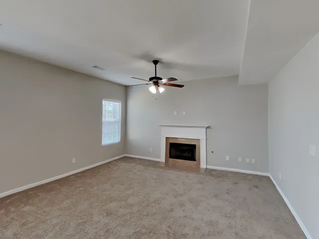 an empty room with chandelier fan and fireplace