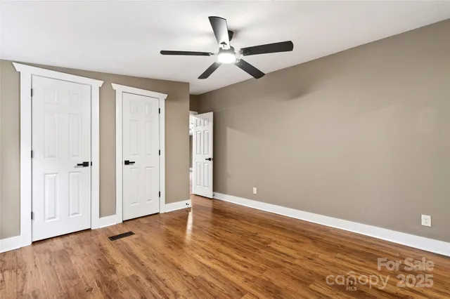 an empty room with wooden floor ceiling fan and windows