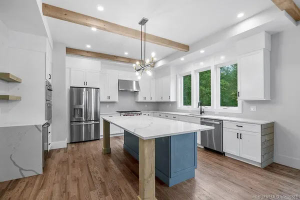 a kitchen with stainless steel appliances a stove a sink dishwasher a refrigerator and white cabinets with wooden floor