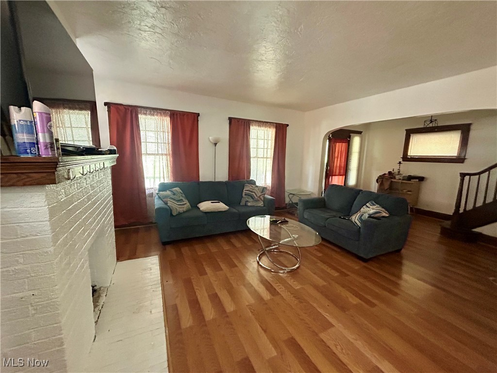 10202 Kinsman Road Cleveland, OH 44104 - Photo 3 of 15 Living area featuring a textured ceiling, stairs, light wood-style flooring, arched walkways, and a brick fireplace