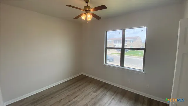 an empty room with wooden floor fan and windows