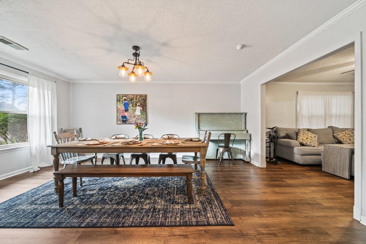 Dining space featuring dark wood-style floors, ornamental molding, a chandelier, and a textured ceiling
