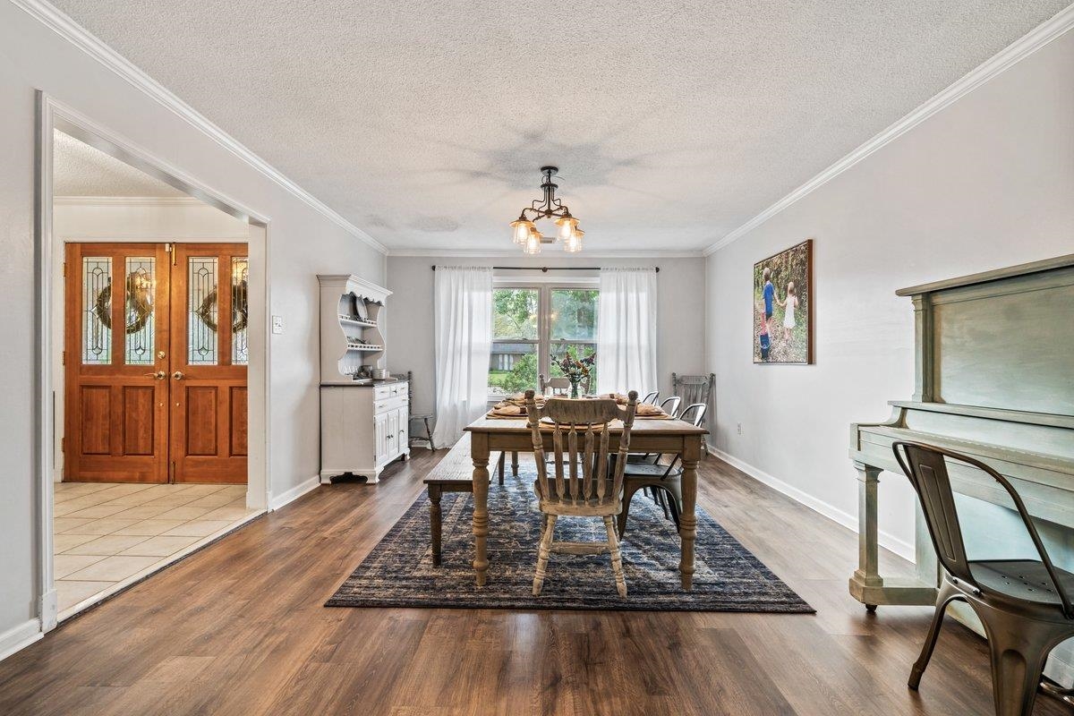 Dining room with a textured ceiling, dark wood-style flooring, ornamental molding, and hanging lights
