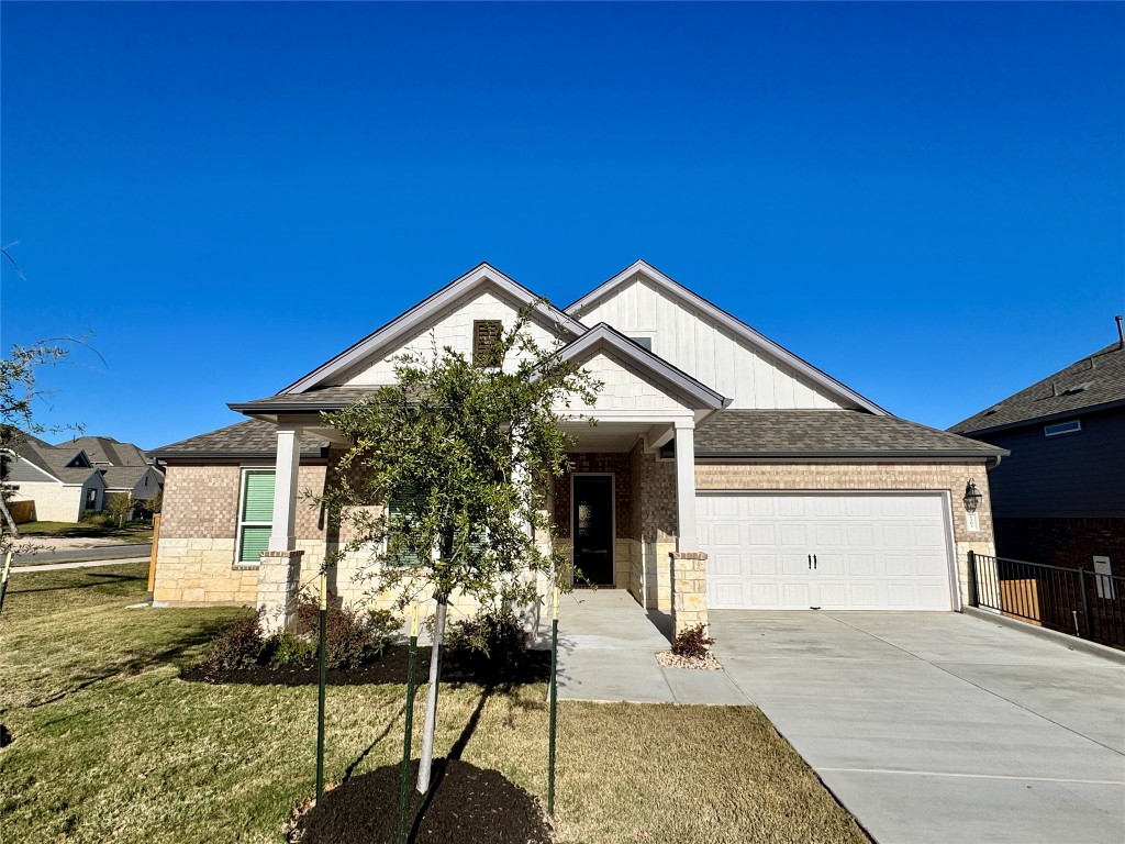 View of front of property with driveway, a front yard, brick siding, a garage, and roof with shingles