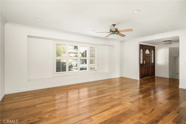 an empty room with wooden floor chandelier fan and windows