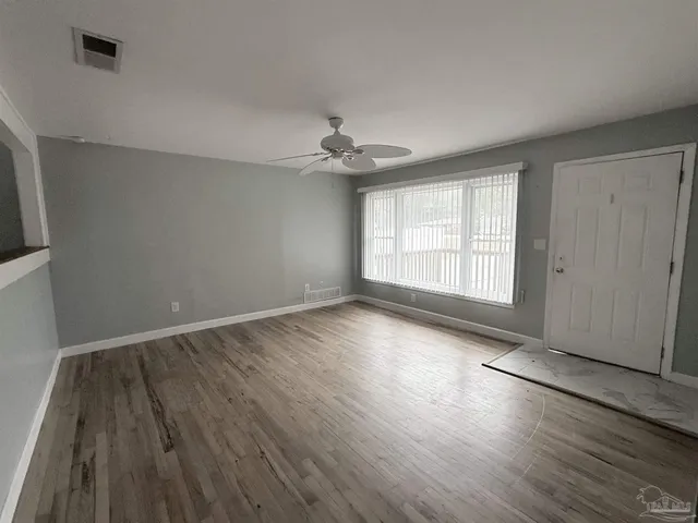 an empty room with wooden floor chandelier fan and windows
