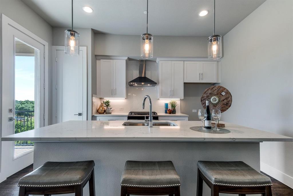 770 North Plano Road, Unit 303 Richardson, TX 75081 - Photo 6 of 26 The kitchen features white cabinetry, a stainless steel range hood, an island with a sink and pendant lighting, and access to a balcony