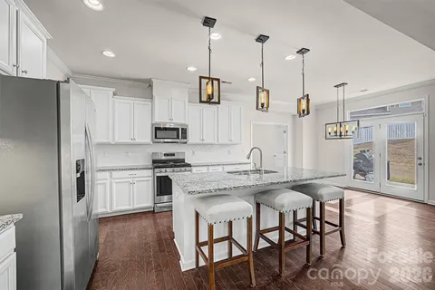 a kitchen with stainless steel appliances granite countertop a sink a stove a refrigerator and island with wooden floor