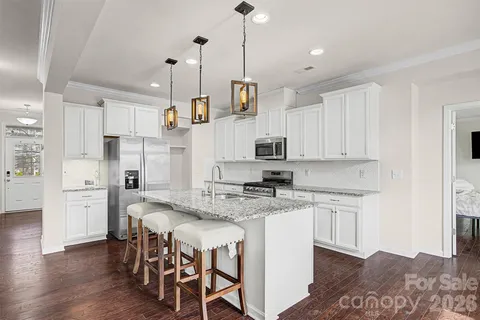 a kitchen with stainless steel appliances granite countertop a stove a sink a refrigerator and white cabinets with wooden floor