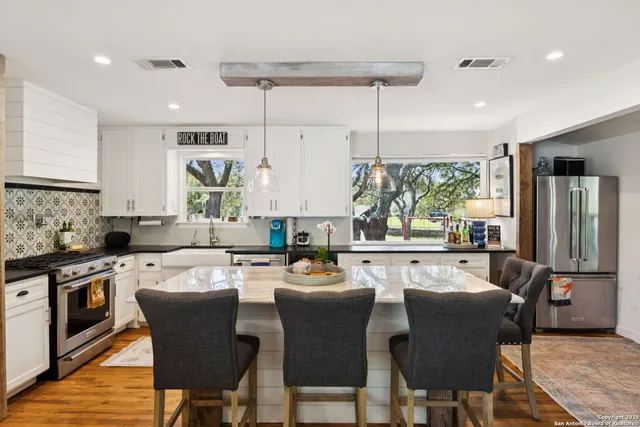 a kitchen with stainless steel appliances granite countertop a stove top oven a sink refrigerator and chairs