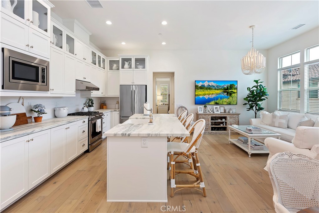 a large white kitchen with stainless steel appliances kitchen island granite countertop a stove a sink a dining table and chairs with wooden floor