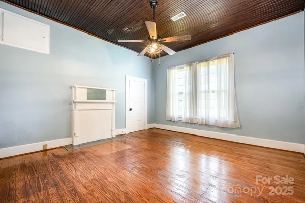 an empty room with wooden floor chandelier fan and windows