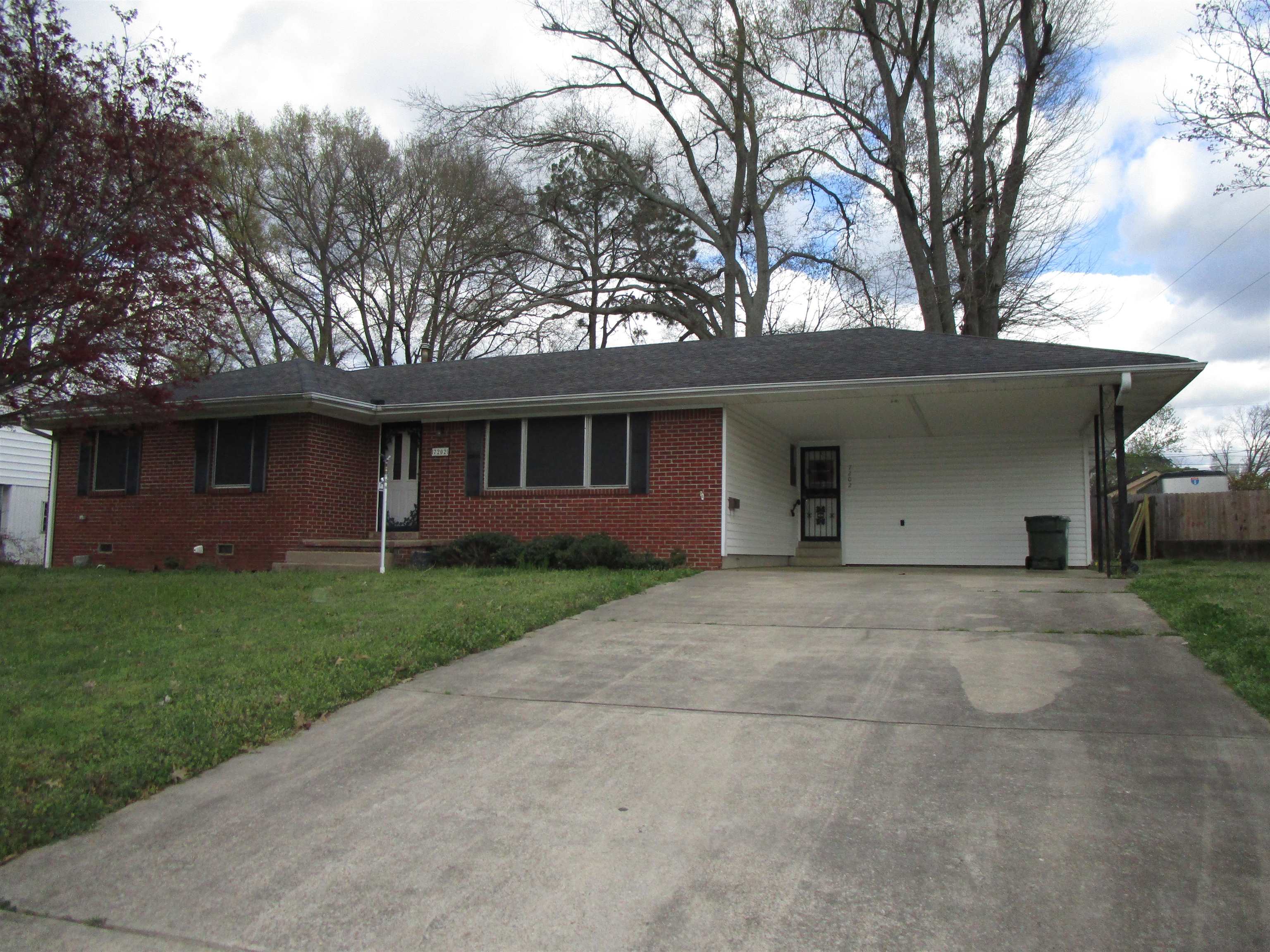 Ranch-style home with a carport, concrete driveway, a front lawn, and brick siding