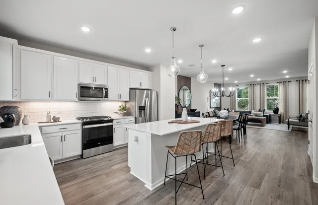 a kitchen with stainless steel appliances a stove top oven a sink a refrigerator white cabinets and chairs with wooden floor