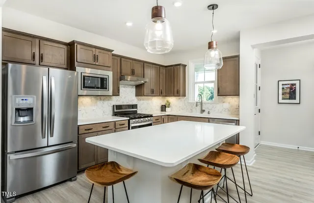 a kitchen with stainless steel appliances granite countertop a stove top oven a sink dishwasher a dining table and chairs with wooden floor