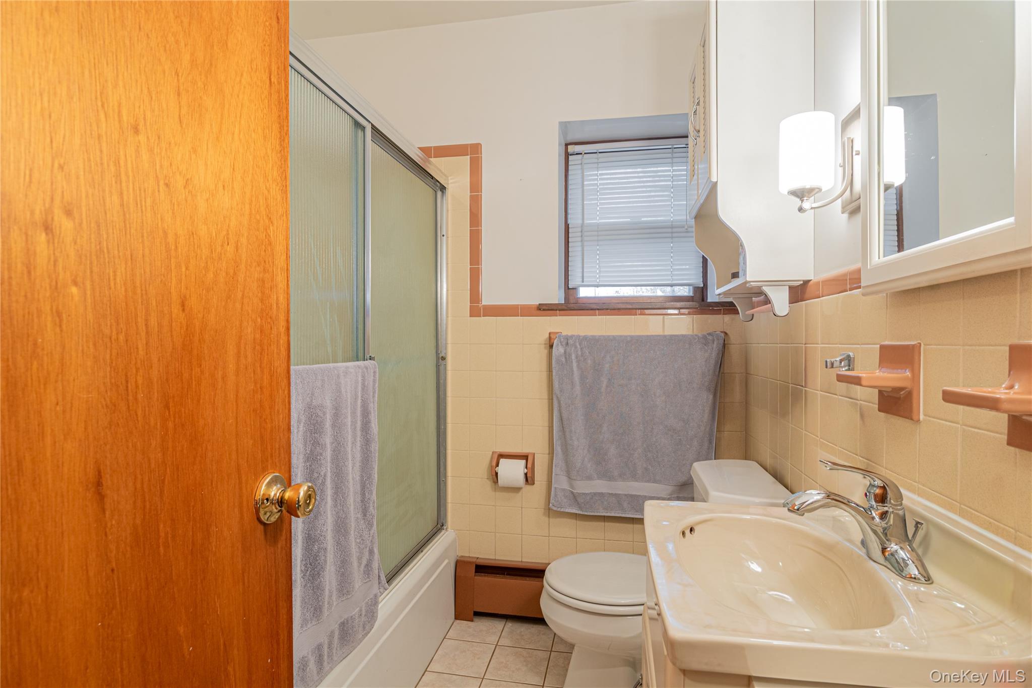 23 Musselman Drive Poughkeepsie, NY 12601 - Photo 25 of 34 Bathroom with light tile patterned floors, baseboard heating, tile walls, vanity, and enclosed tub / shower combo