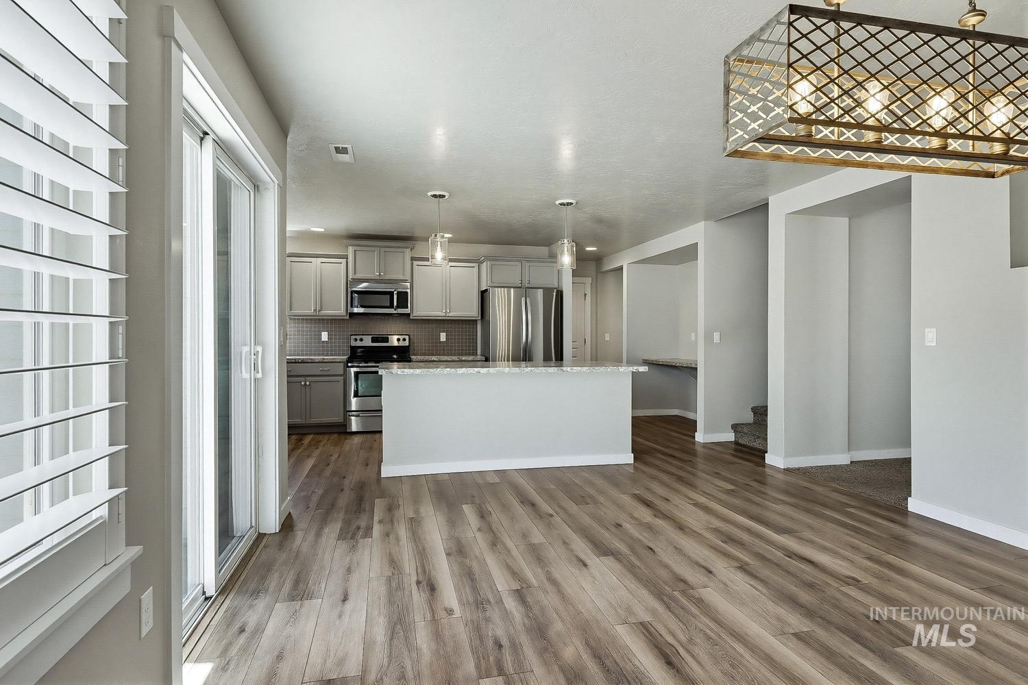 846 North Hidden View Way Star, ID 83669 - Photo 18 of 49 Open concept interior featuring wood-finish flooring, a kitchen island with stone-finish countertop, stainless steel appliances, and a decorative ceiling light fixture