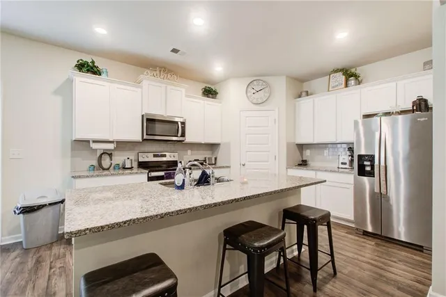 a kitchen with granite countertop kitchen island white cabinets appliances and wooden floor